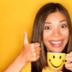 Student doing thumbs up with yellow coffee mug on a yellow background